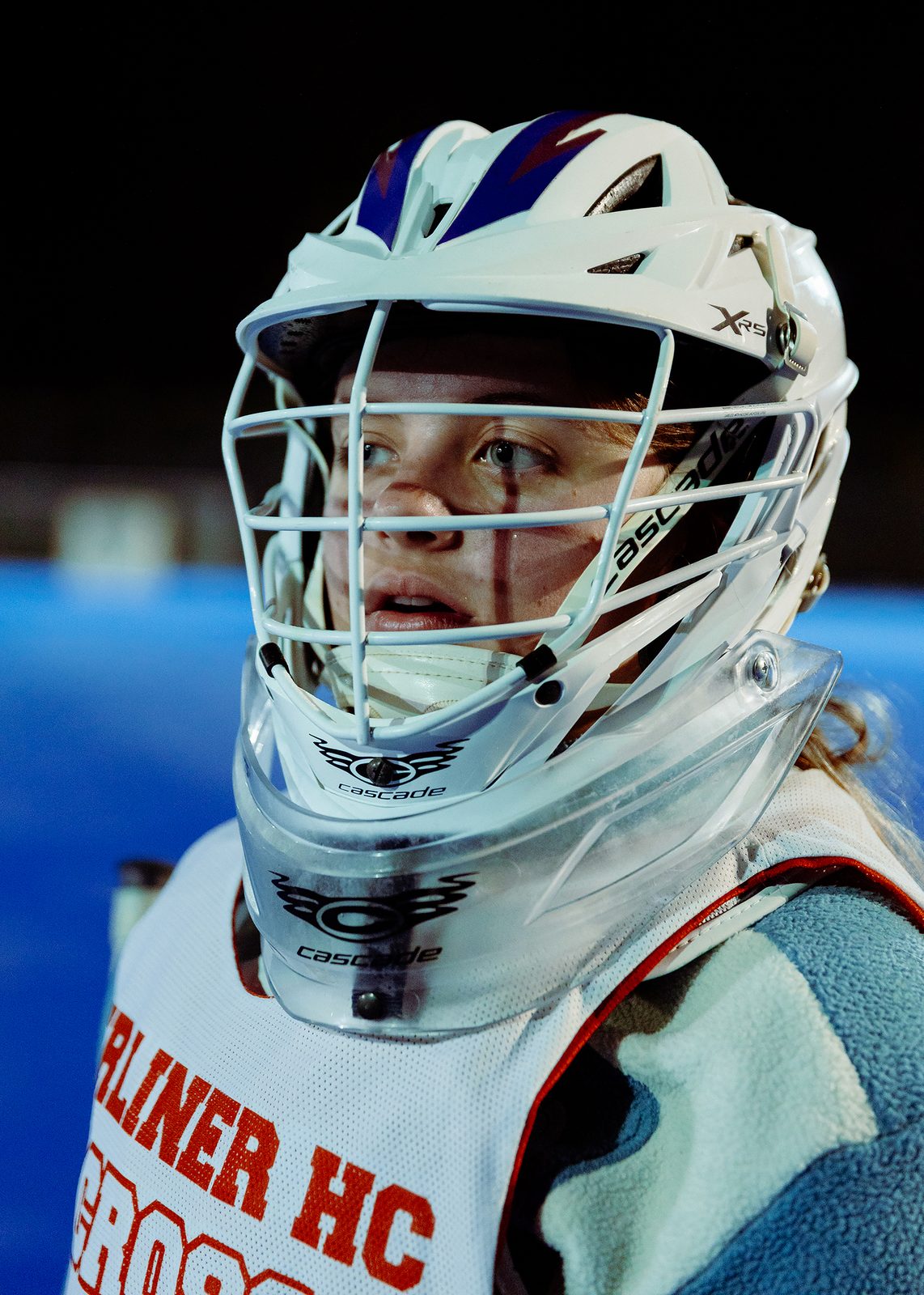 Documentary photograph of a young female lacrosse player behind the protective cage of her helmet. Lacrosse by Pia Henkel, Woman Portrait Gallery.