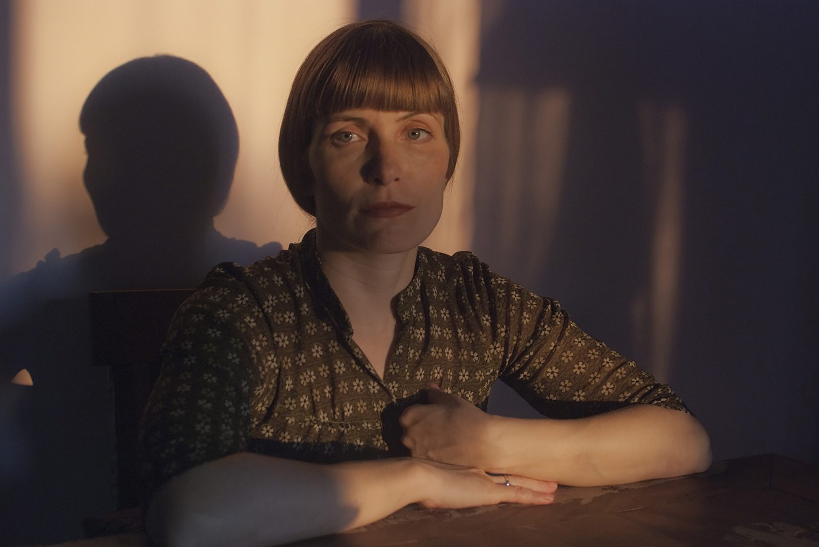 Carefully staged sepia-toned photograph of a woman with a precise hairstyle sitting at a table, soft natural light illuminating the composed controlled scene. Inspired by Ingmar Bergman film Persona. Persona by Vassilis Konstantinou, Woman Portrait Gallery.